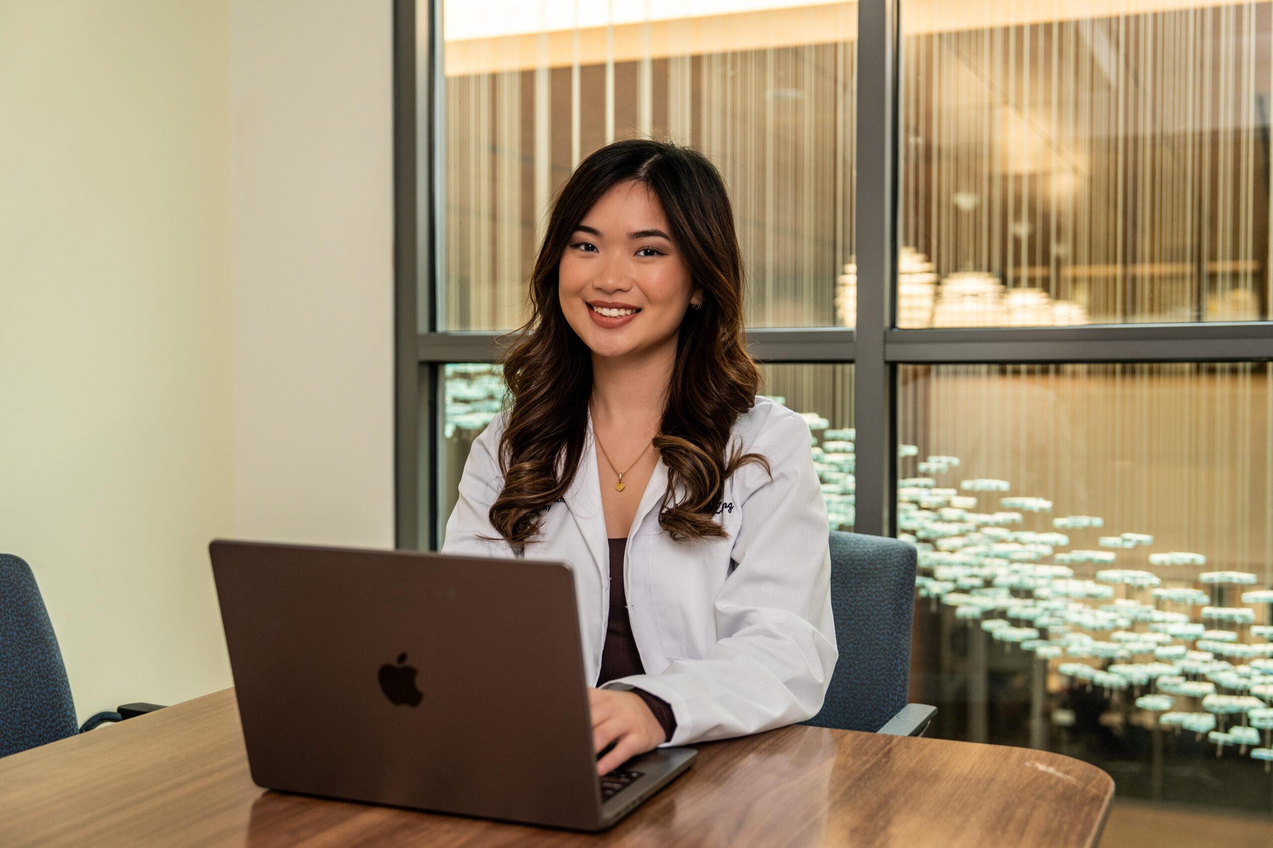 Female student in white lab coat sitting at laptop.